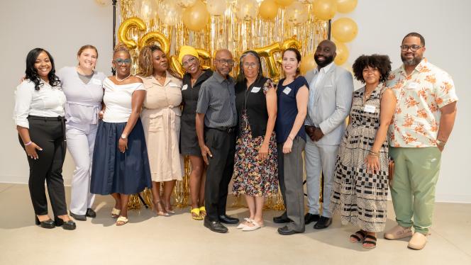 Group photo of the participants and staff of the REACH Fellowship program at their graduation ceremony, with gold streamers and "Congrats" balloon
