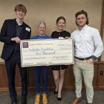 Three students stand with organization representative and display large check of grant-awarded funds