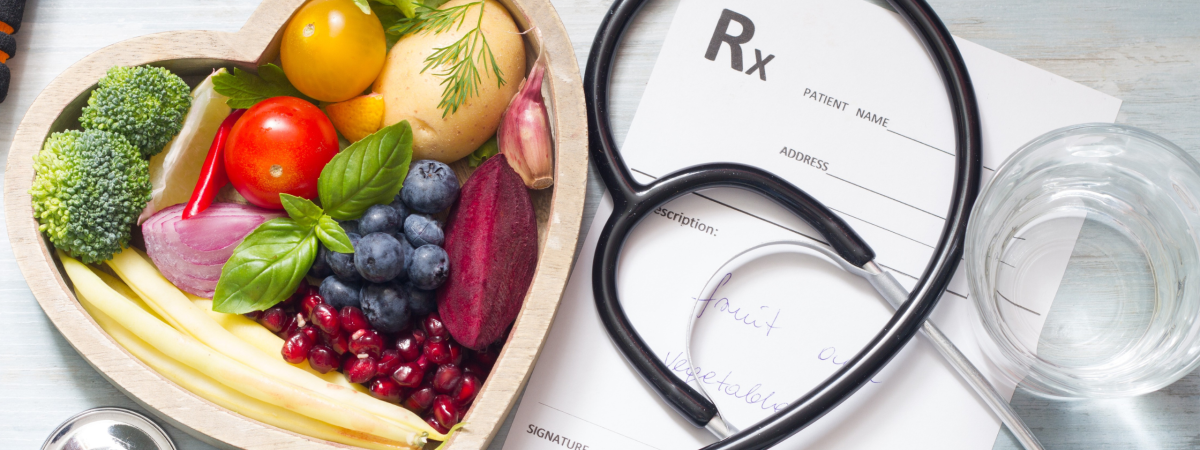 heart-shaped bowl filled with fruits and vegetables, next to a prescription pad and a stethoscope