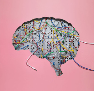 A brain shaped circuit with wires attached on a pink background