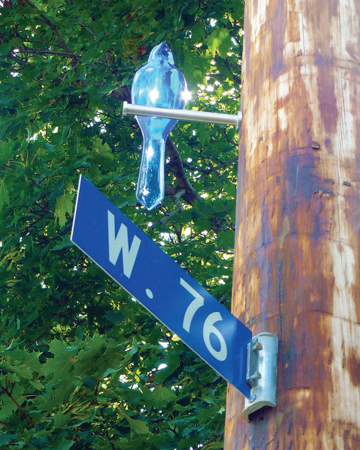 A glassy bluebird sculpture perched above the W. 76 street sign