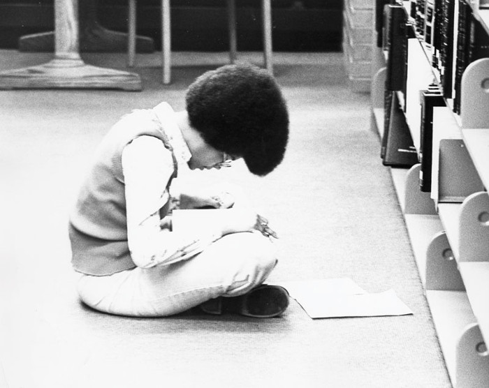 A black and white photo of a young person reading cross-legged.