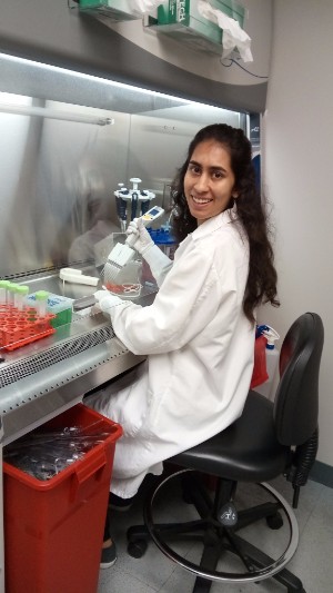 A female student in a lab coat seated and doing work in a genetics lab.