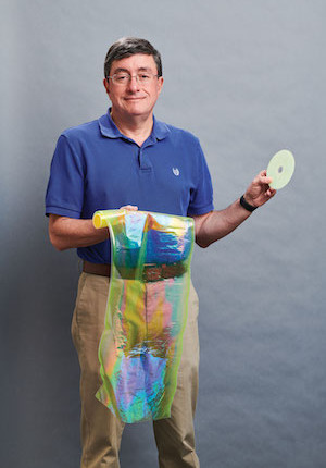 Case Western Reserve University Professor Kenneth Singer holding a roll of polymer film and a CD.