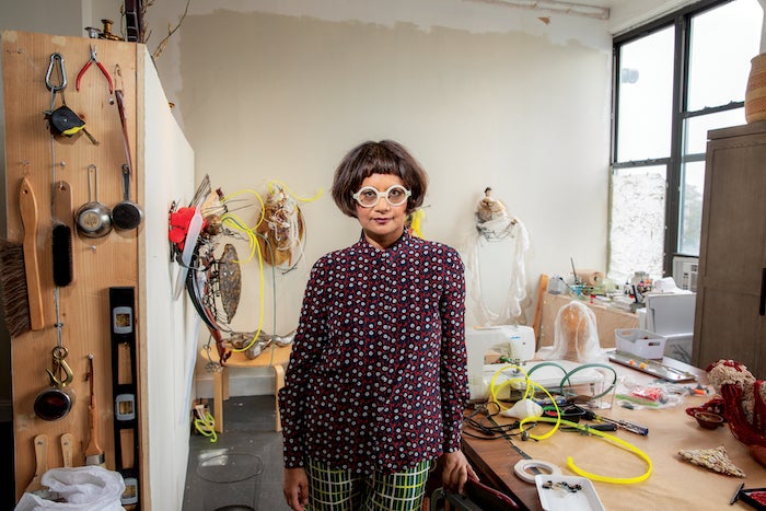 Photo of Rina Banerjee standing in front of her artwork