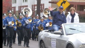 Barbara Snyder rides on the back of a car with Fred DiSanto as they are followed by the university marching band.