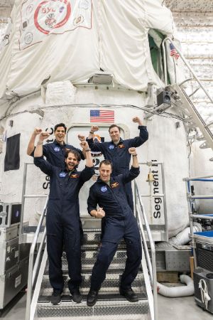 Photo of four men standing in front of a space simulation habitat with raised arms.