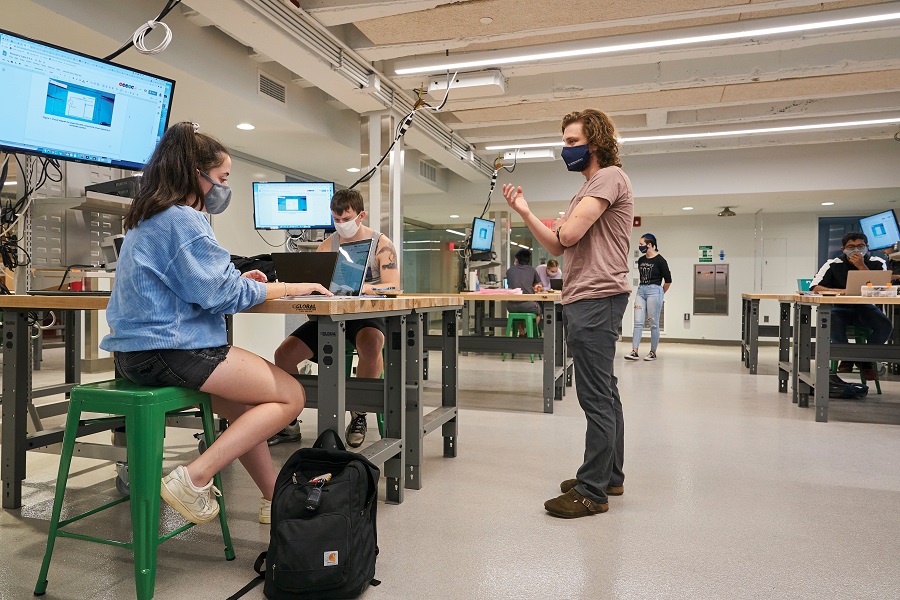 Image of students wearing masks in a lab, on laptops and having a discussion.