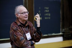 Photo of Donald E. Knuth holding a piece of chalk in front of a chalkboard.