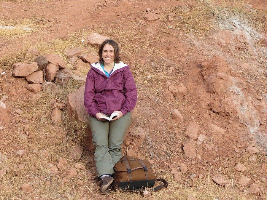 Image of Beverly Saylor sitting on a rock and holding a book open.