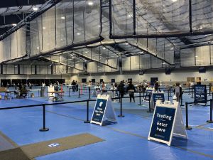 Signs for COVID-19 testing sit in front of a queue area, which has been set up inside a recreation and athletic center.