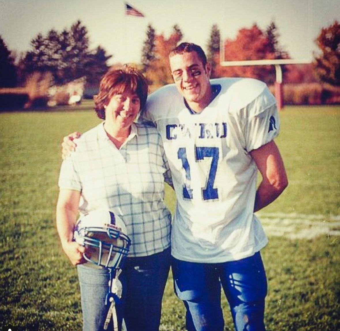 A young John Kobs in a football jersey standing with his mother