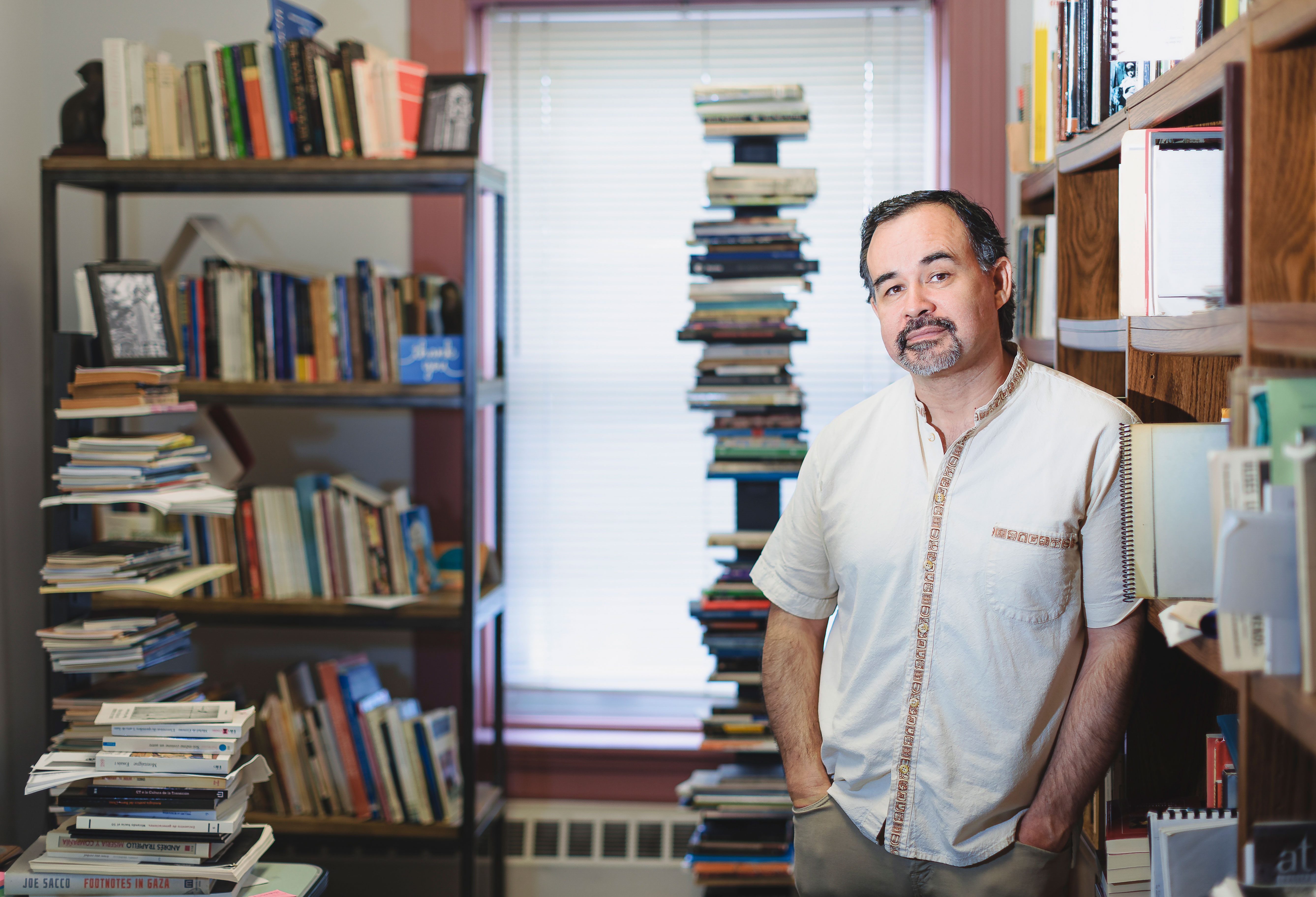 Cristián Gómez Olivares standing in his office amongst stacks of books and bookshelves