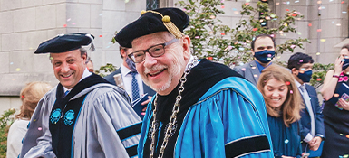President Eric Kaler walking among faculty and staff wearing commencement robes.