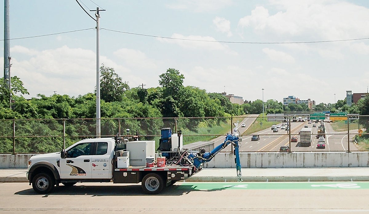 Photo of a operator-driven, truck-mounted mobile robotic pavement-marking system marking a road.