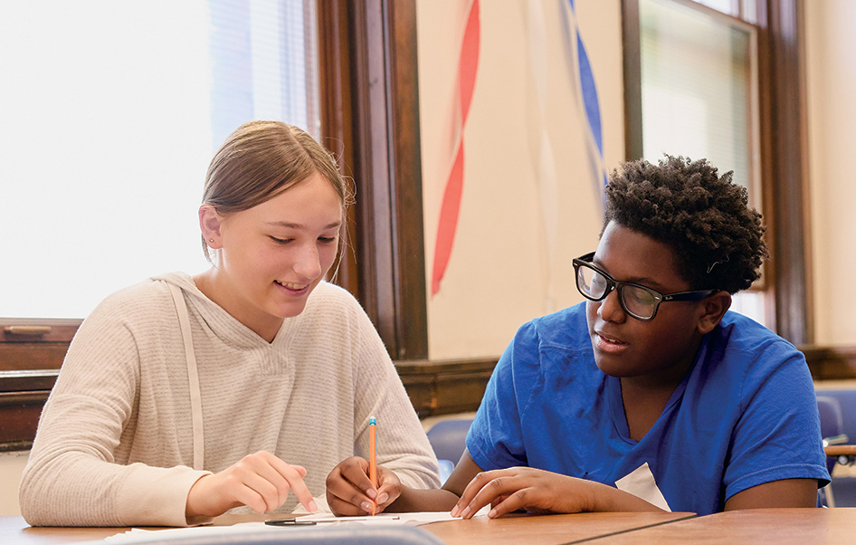 A high school student helps a middle-school student with math problems during a summer camp.