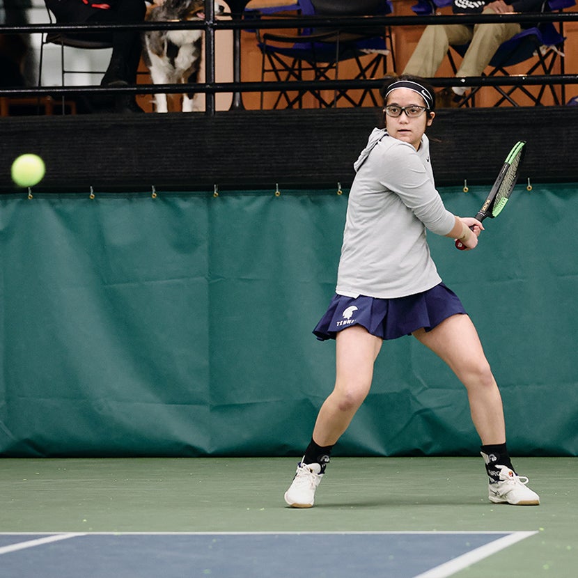 Hannah Kassaie on a tennis court and preparing to hit a ball.