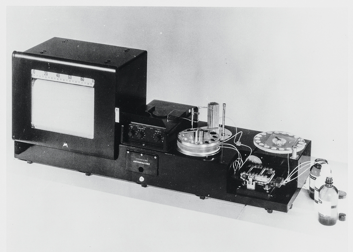 A black and white image of a piece of equipment called an analyzer that has a measuring box sitting atop a long rectangular part of the equipment with several features.