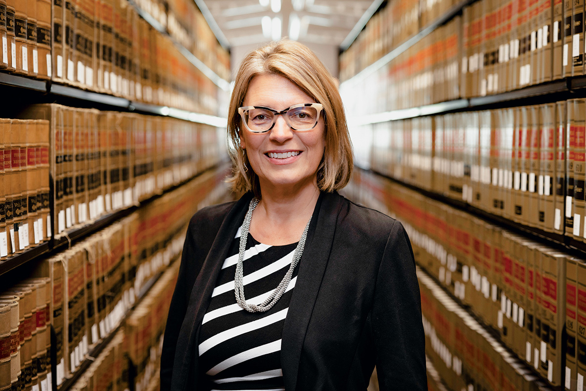 A photo of Professor Jessie Hill standing in a library aisle and flanked by shelves of law books.