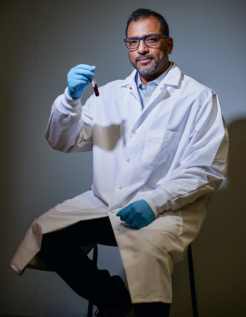 A photo portrait of Biomedical Engineer Anirban Sen Gupta seated, wearing a lab coat and holding a vial of blood.