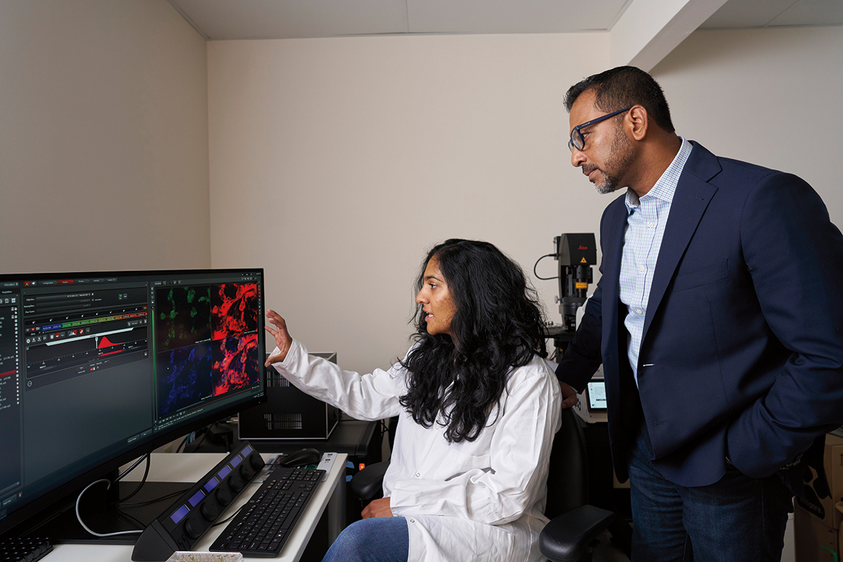 Two researchers in a lab looking at a computer, one is seated and the other standing.