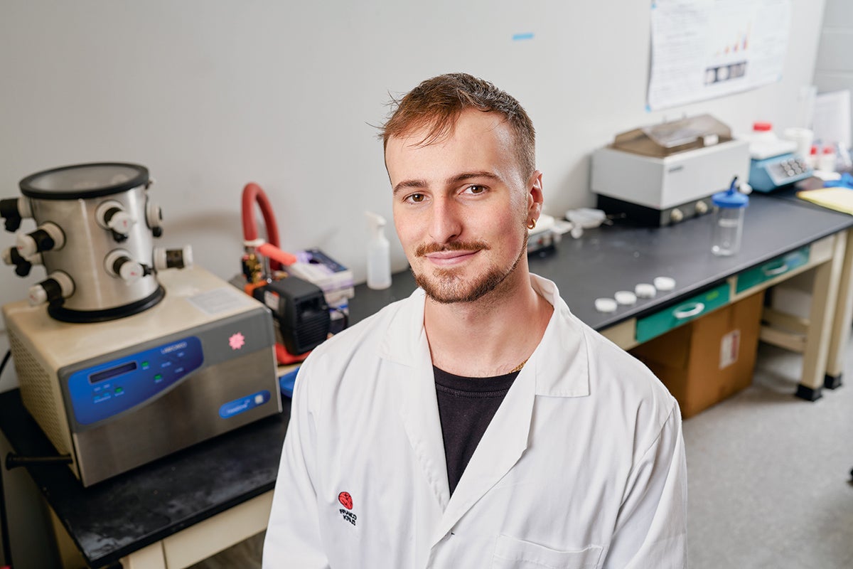 An image of Franco Kraiselburd in a lab with equipment on a table behind him.