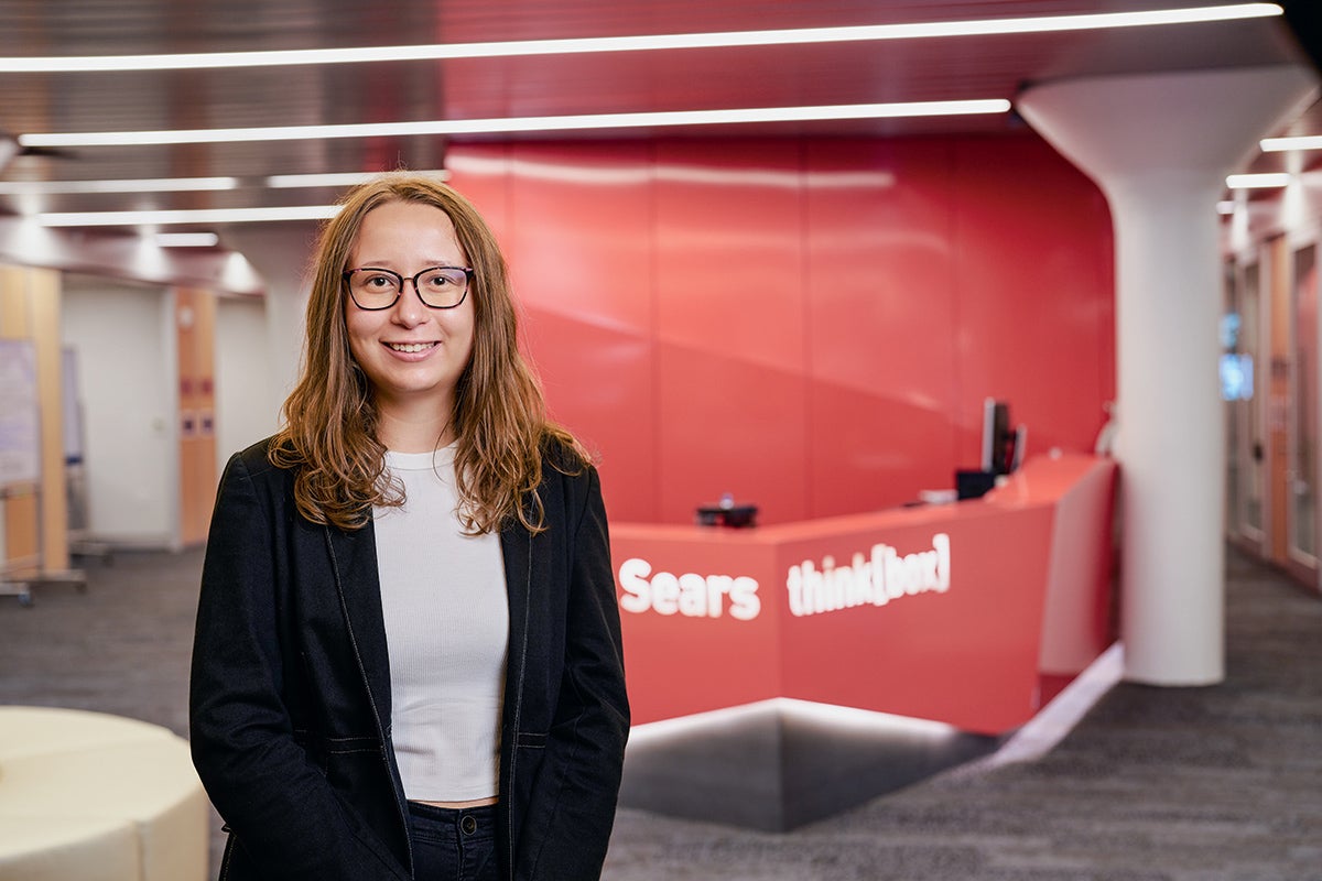 Student Evelyn Urbancsok standing in front of a red reception desk with the name Sears think[box] in large, white letters.