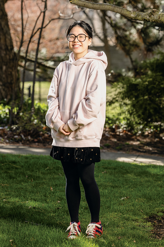 Photo portrait of a student with hands clasped together standing outside by a tree.