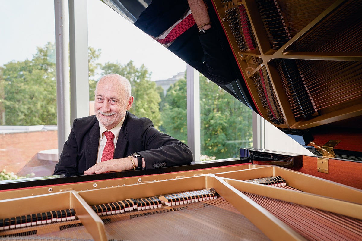 A professor, who also is a pianist, sitting at a piano, framed by the piano and the raised lid.