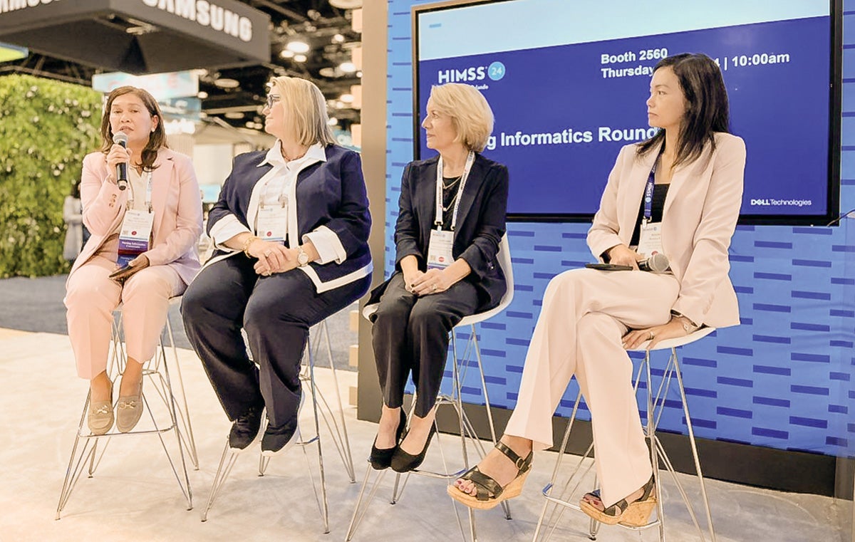 Four people seated in front of an audience for a panel. One is talking and holding a microphone.