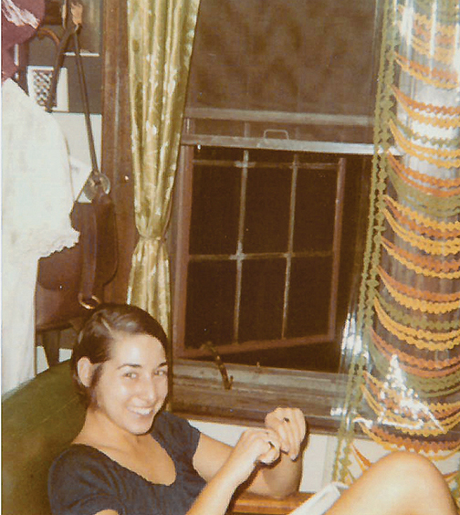 A student in a residence hall in 1970, smiling and seated next to an open window.