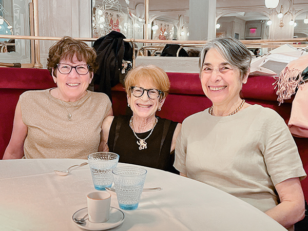 Three people sitting in a restaurant booth and smiling brightly.