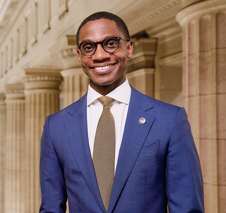 Cleveland Mayor Justin Bibb standing on the second floor of city hall with pillars and a view of the rotunda behind him.