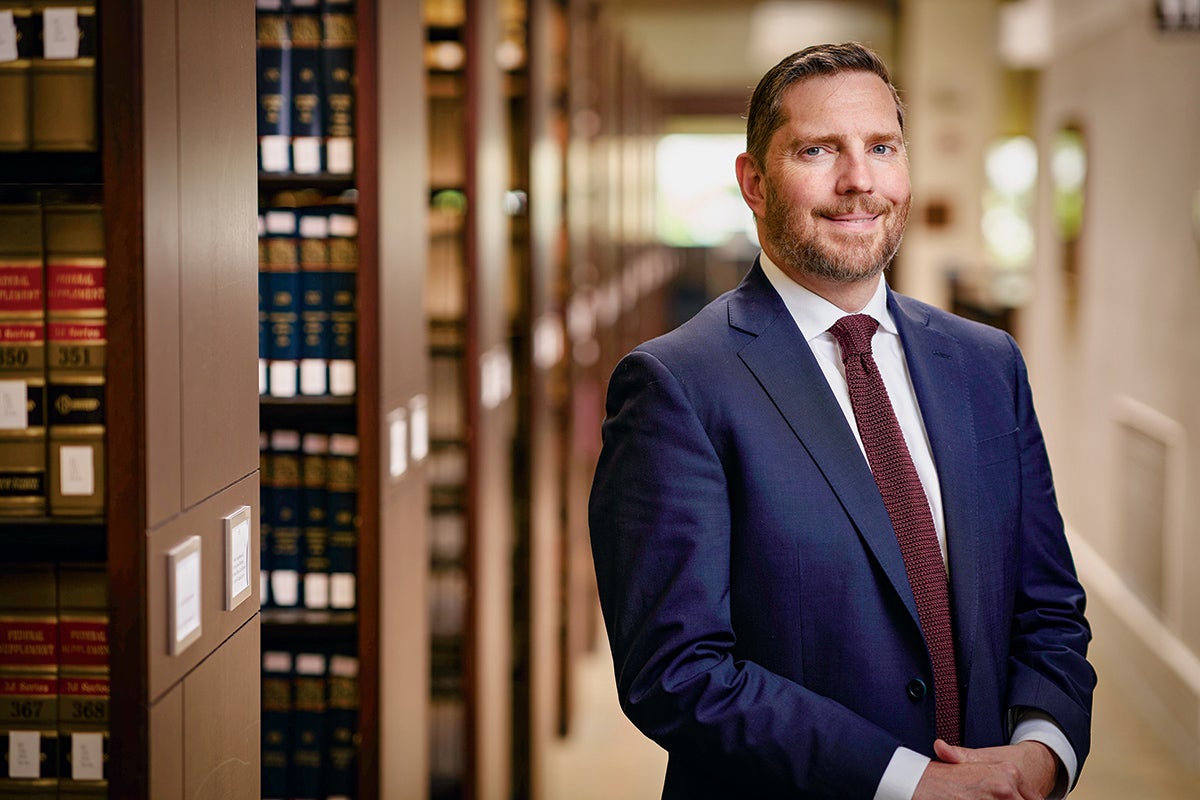 Portrait photo of Paul Rose in the School of Law library with stacks of books behind him.