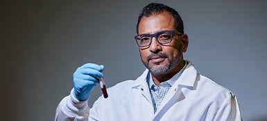 A photo portrait of Biomedical Engineer Anirban Sen Gupta seated, wearing a lab coat and holding a vial of blood.