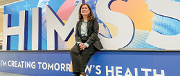 Mary Joy Garcia-Dia casually sits in front of a large sign for the Healthcare Information and Management Systems Society conference, where she spoke.