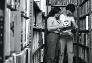 B&W--two students looking at a record in front of a shelf full of records.