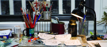 Bachtell’s desk, adorned with mugs full of paintbrushes, a black lamp and his drawings.