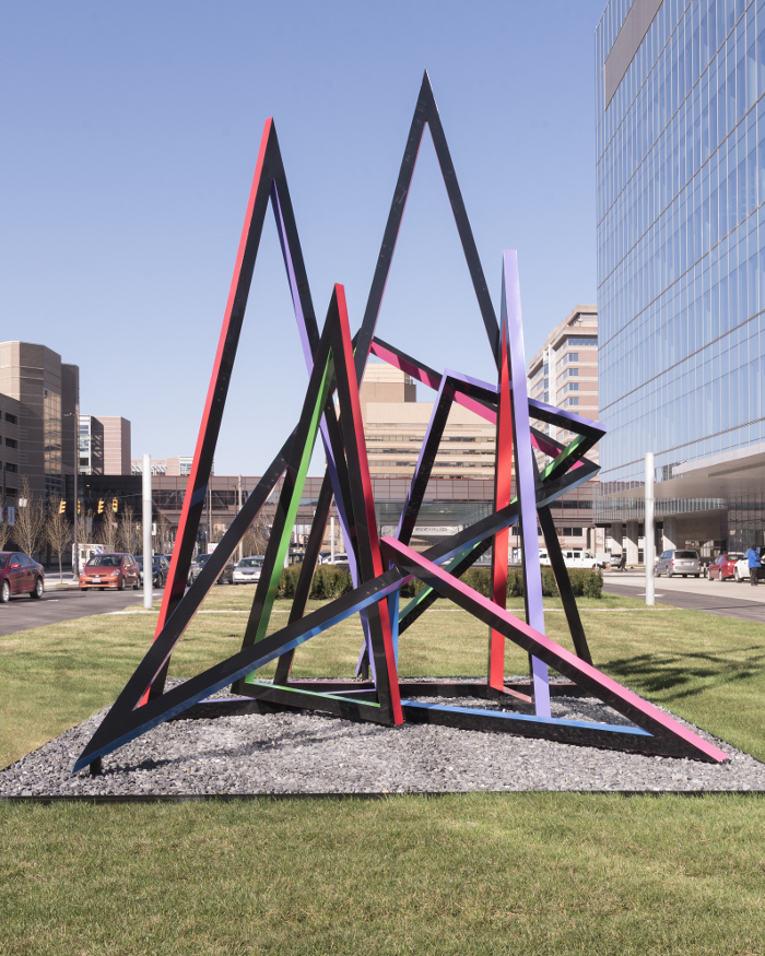 A large painted aluminum structure forming various sharp edges located outside in a green-space aluminum