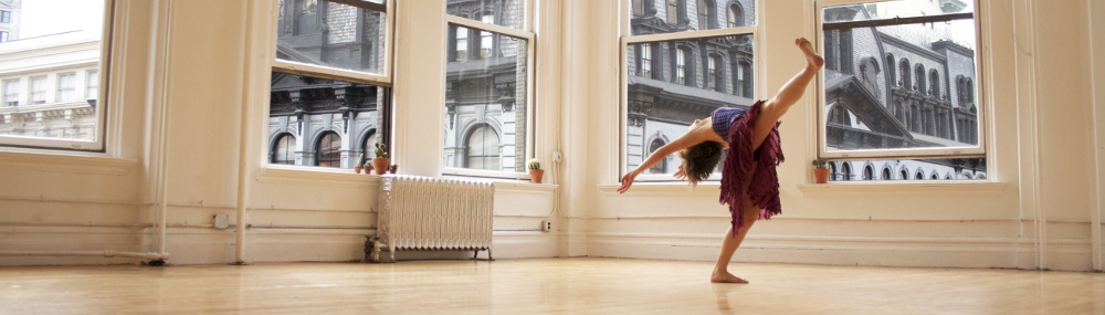 A dancing arching back in a dance studio with giant windows.