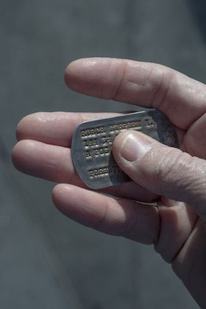 An image of a hand holding a military dogtag with the name 