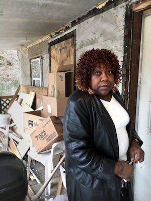 Image of a woman named Iris Tyler standing in front of a house with piles of cardboard boxes in front