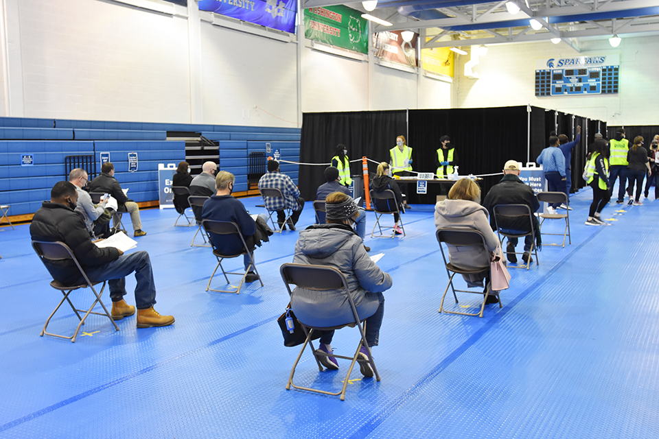 Image of people waiting to receive their vaccines in a gymnasium