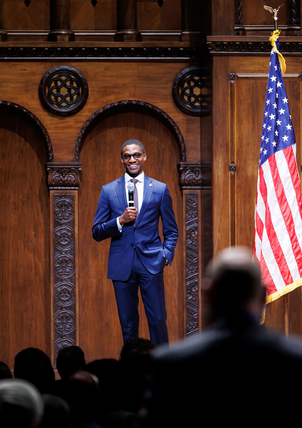 Justin Bibb holding a microphone while standing on a stage, smiling out at the audience.