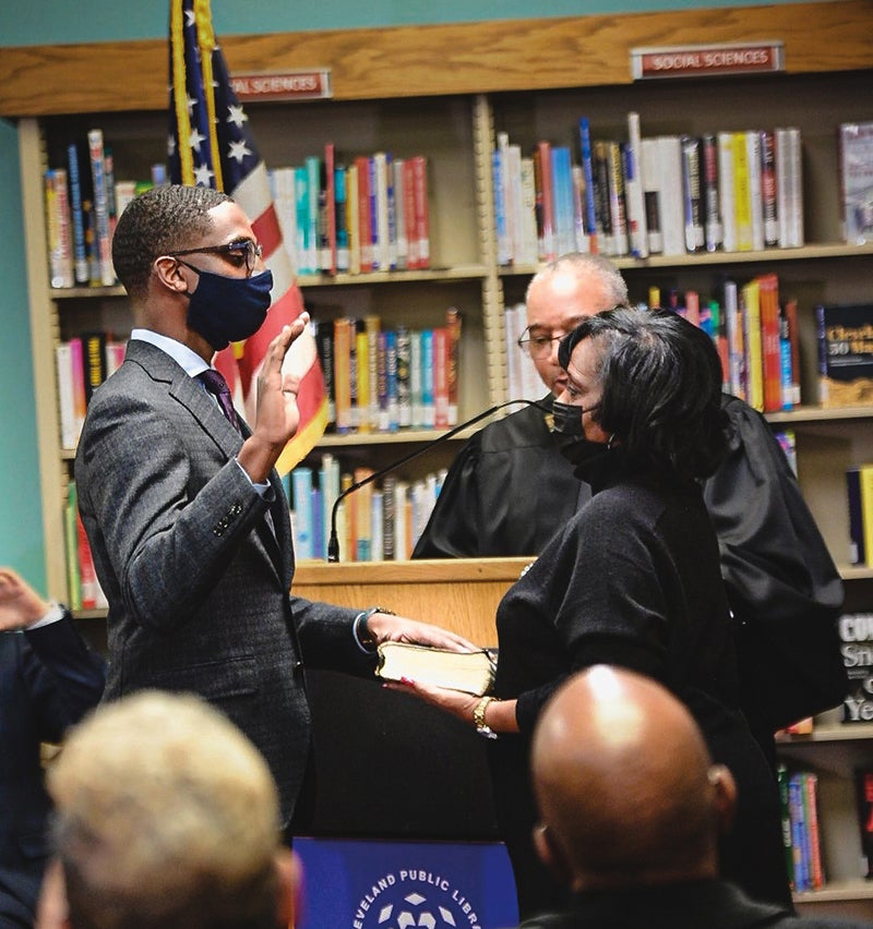 Justin Bibb being sworn in as Cleveland mayor, his left hand over a Bible. His mother is holding the Bible.