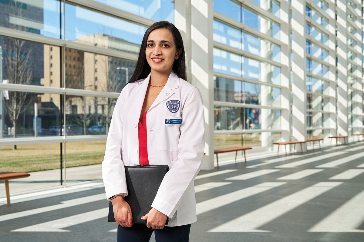 Medical student Maira Bhatty in a white coat holding a leather portfolio