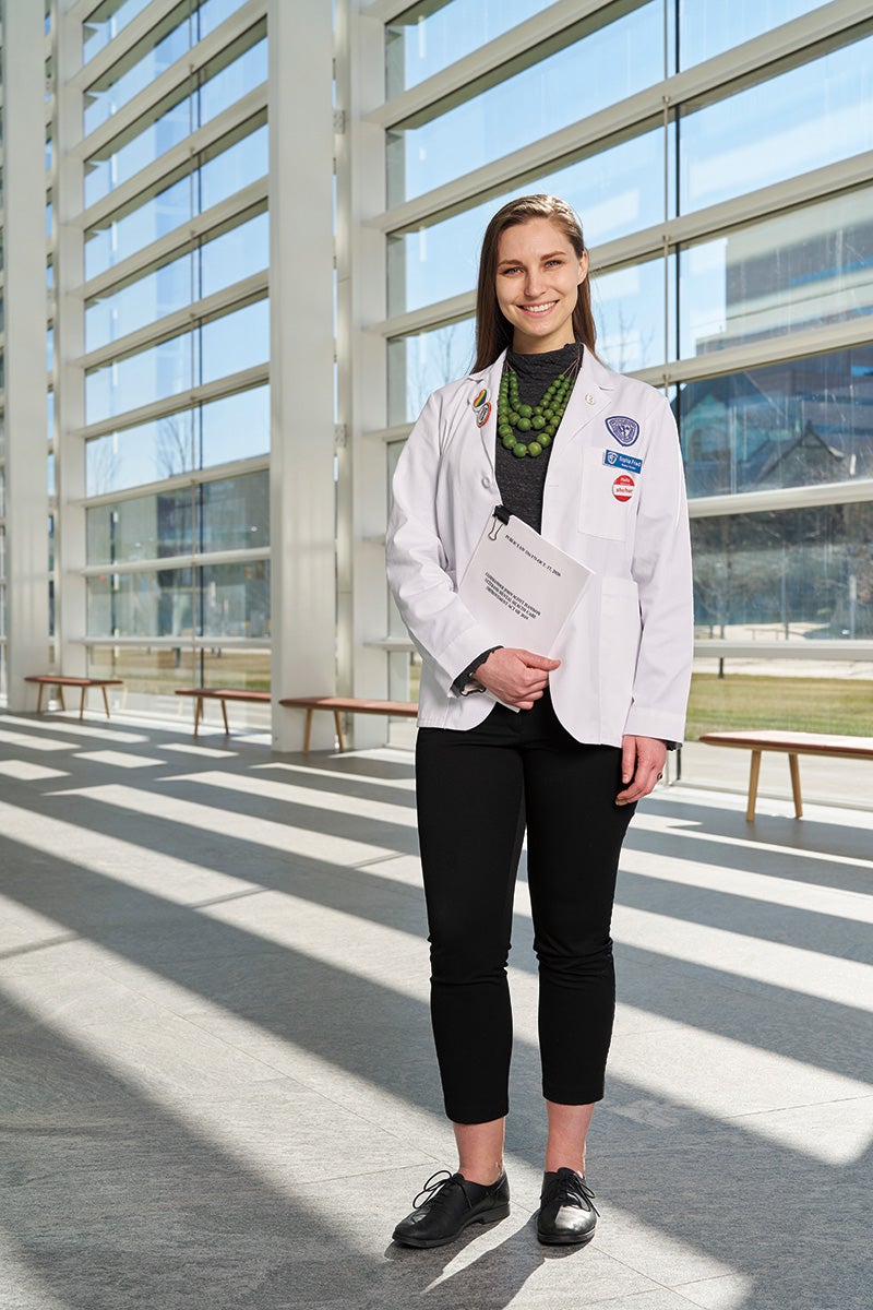 Medical student Sophie Friedl in a white coat holding a copy of a federal law
