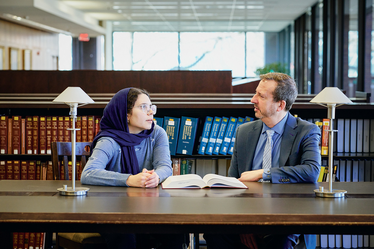 A law student and professor meeting in a school library and discuss cases.