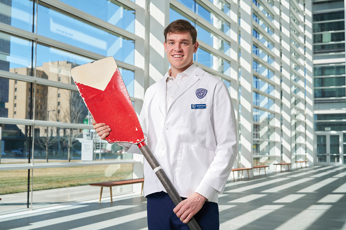 Medical student Alexander Richards in a white coat holding an oar blade used to row