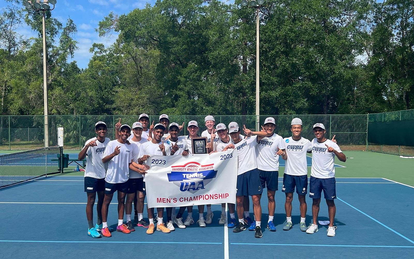 The men’s tennis team in a group photo holding a large sign showing they are won the University Athletic Associationship Championship.